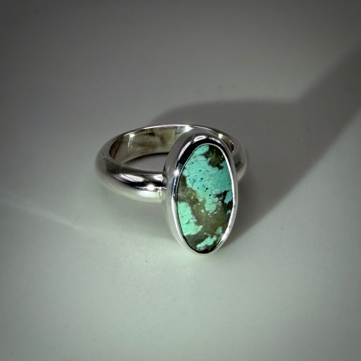 A sterling silver ring featuring an oval turquoise stone with prominent brown matrix, set against a neutral gray background.
