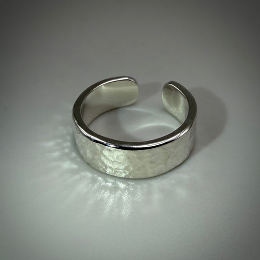 A wide silver cuff ring with a hammered texture on the front and polished beveled edges, photographed on a neutral gray background.