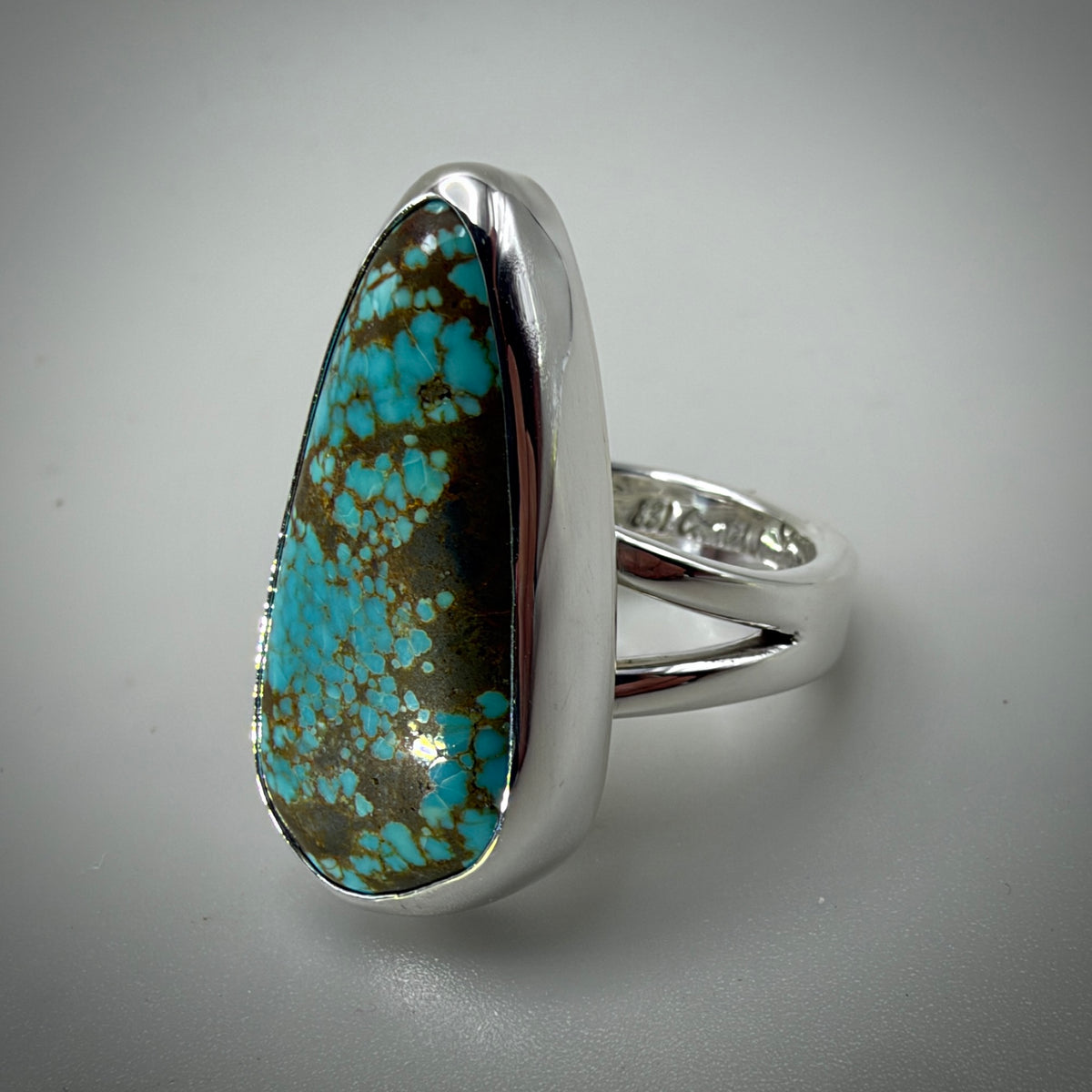 A silver ring featuring a large, teardrop-shaped turquoise stone with brown matrix, set in a polished silver band on a neutral gray background.