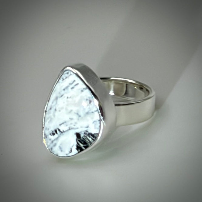 A silver ring featuring a large, irregular teardrop-shaped white stone with black marbled or textured inclusions, set in a polished silver bezel on a neutral gray background.