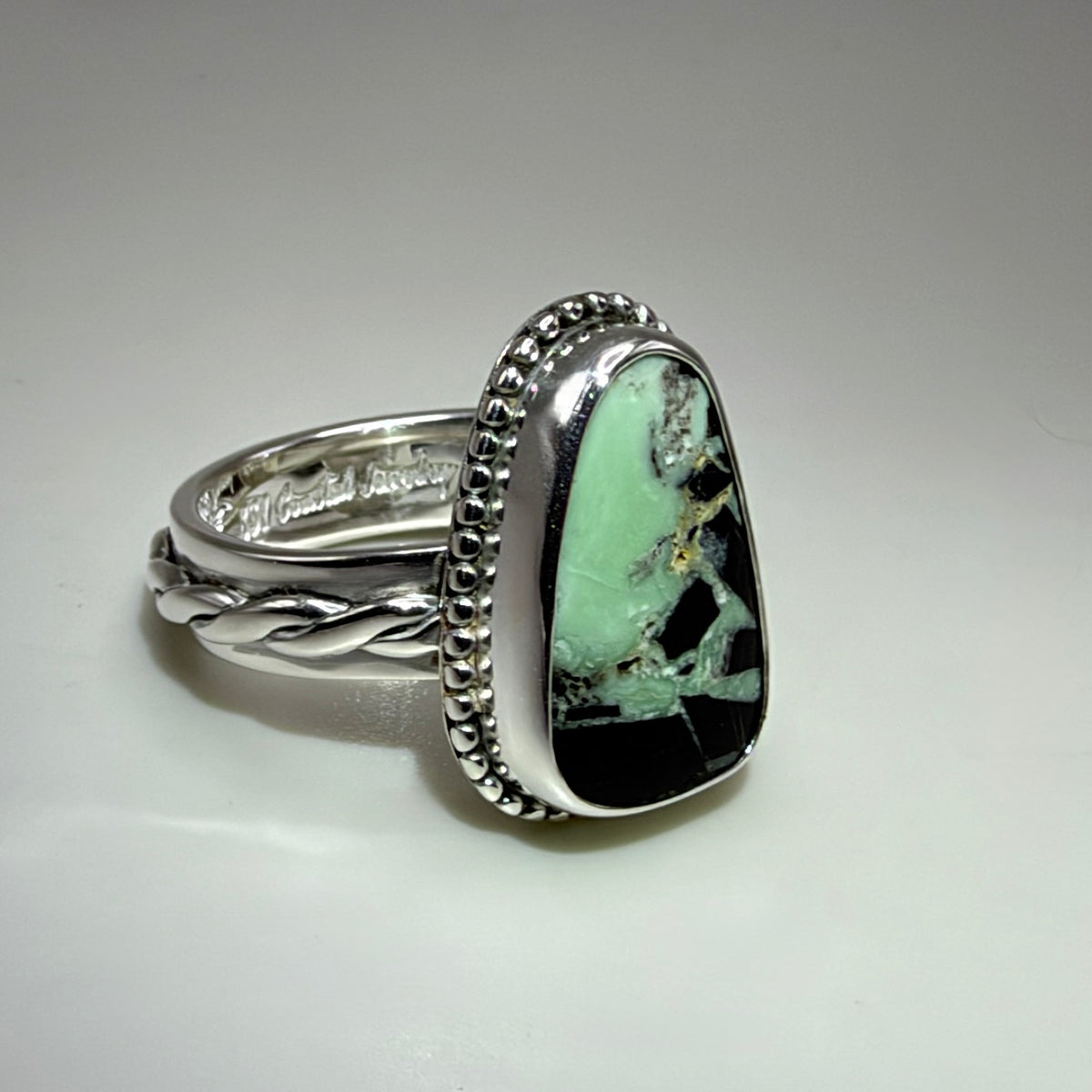 A sterling silver ring featuring a large, irregular-shaped turquoise stone with black and green matrix patterns, set in a decorative bezel and a twisted band.
